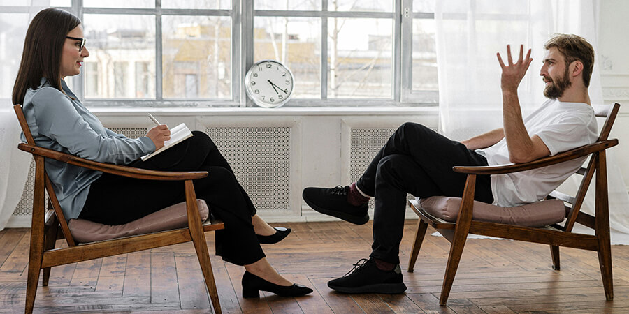 Counselling session - woman with notepad and man in white tee-shirt.