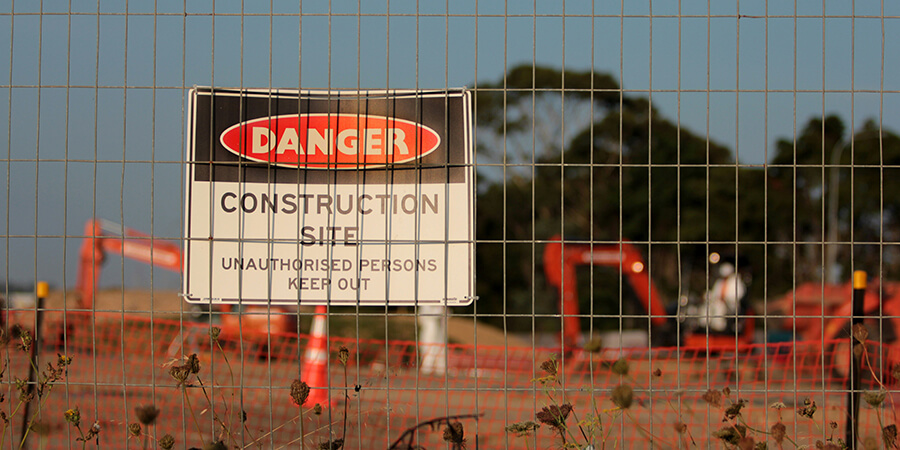 Danger Construction Site sign behind a metal fence.