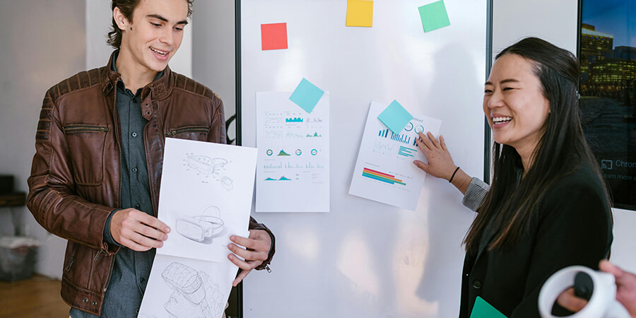 Two people presenting a design standing by a whiteboard.