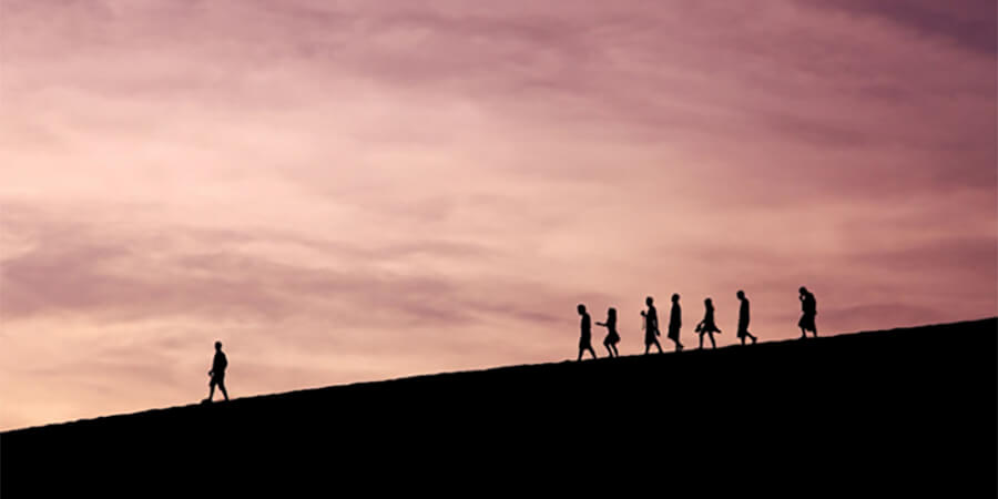 Silhouette of leader walking down a hill at sunset with followers behind.