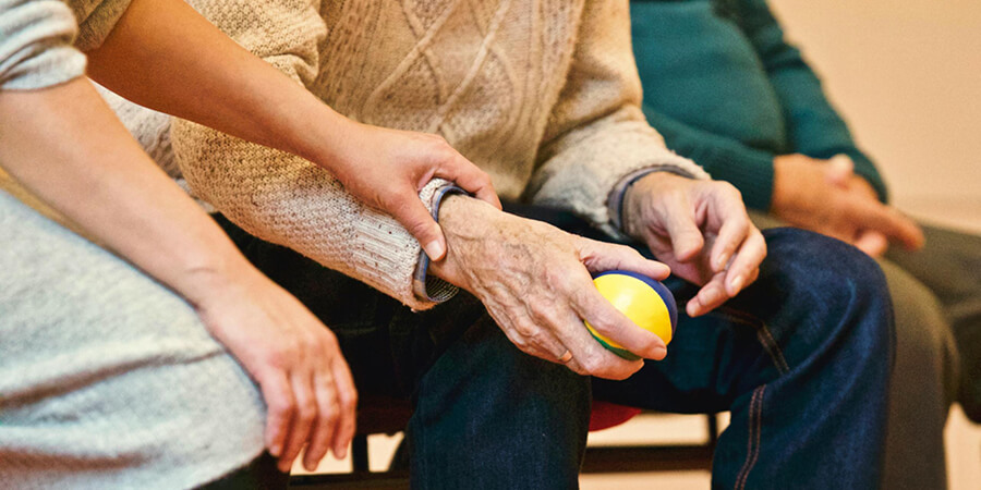 Nurse holding the wrist of an elderly man holding a ball.