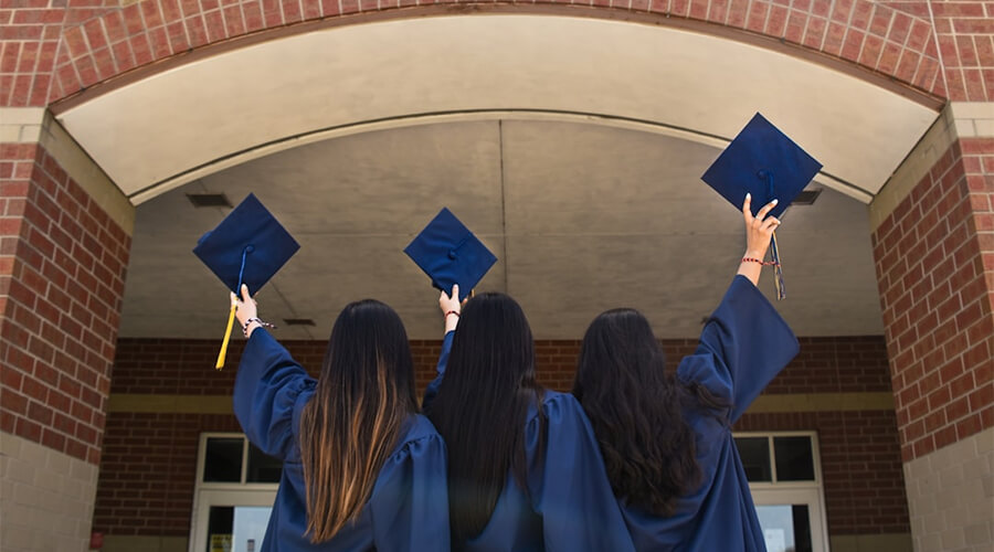 Graduates in blue gowns holding up their mortar boards