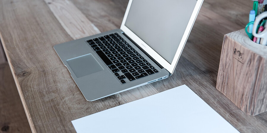 Laptop on a wooden desk with some paper in a home office.