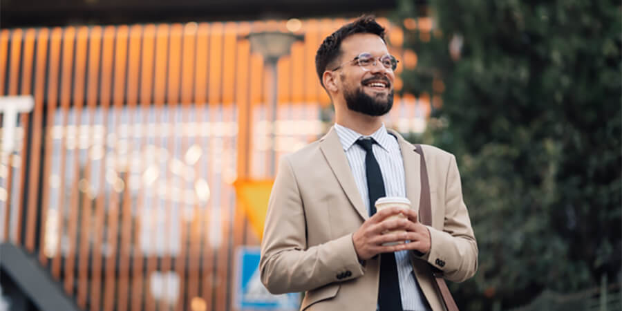 Smiling man in a suit holding a take out coffee.