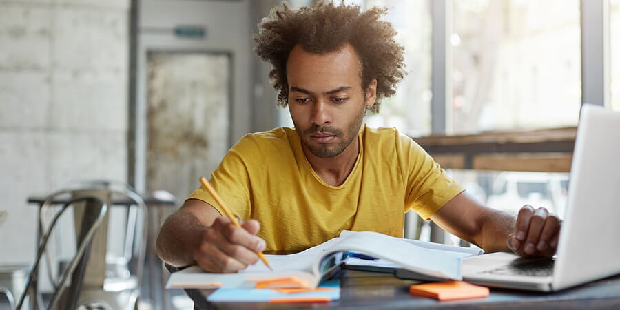 Man studying at a desk with a laptop and notepad.