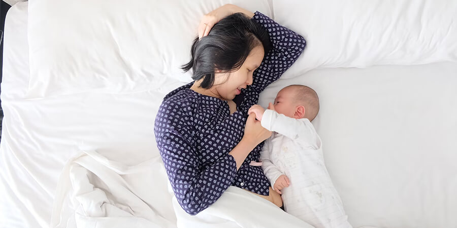 Mother and baby laying on a bed.