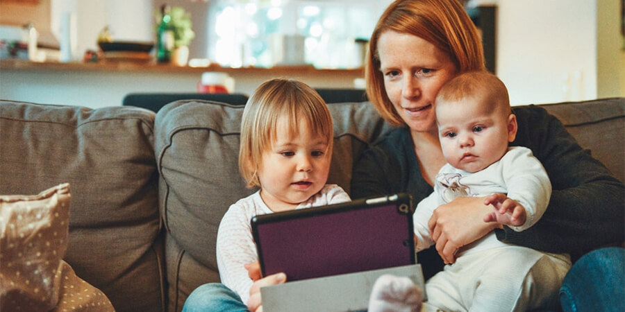 Mother and young daughters on a sofa looking at a tablet