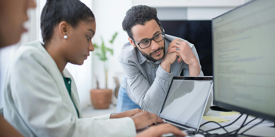 Man looking at code on a screen while a woman types.