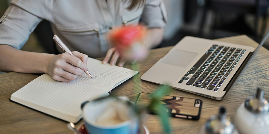 Woman writing in a notepad on a desk.