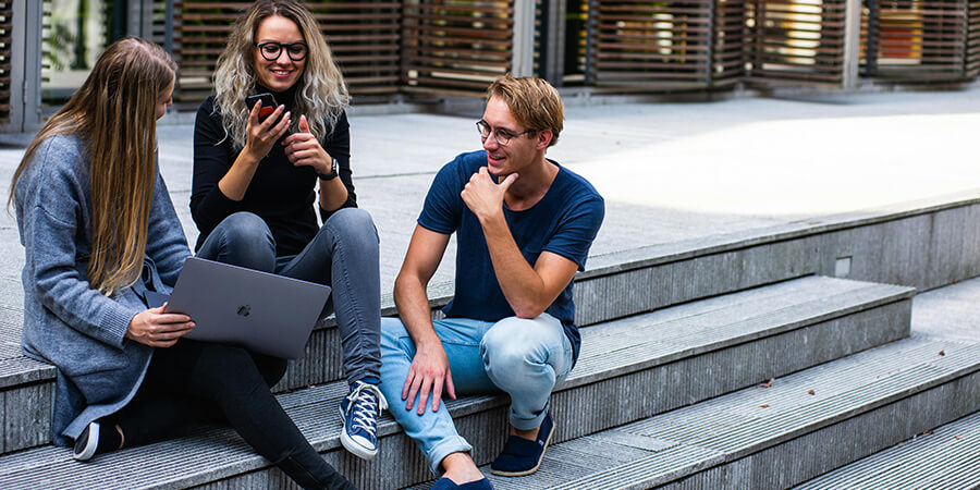 Student group sitting on steps with phone and laptop.