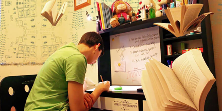 Student working at a desk with books flying around.