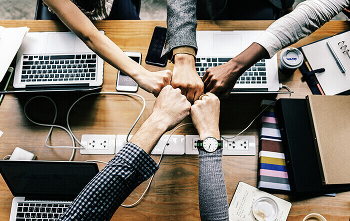 Group of people fist bumping over laptops.
