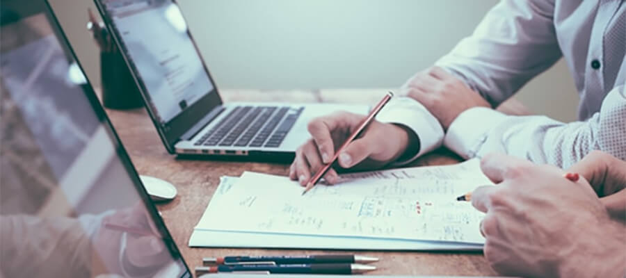 Businessmen working on paper with laptops in the background.
