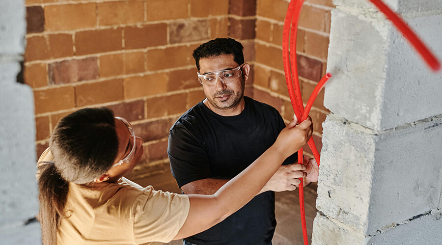 Tradespeople with safety glasses holding a red pipe.