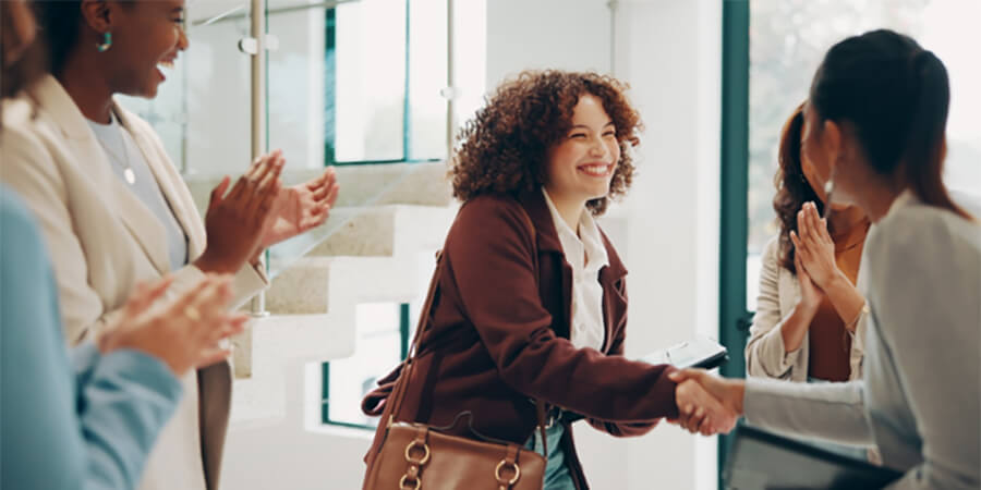 Smiling woman shaking hands with someone while being welcomed into a team.