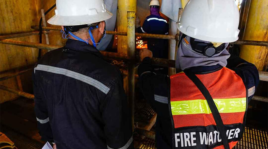 The back of safety officers including a 'Fire Watcher' in an industrial setting.